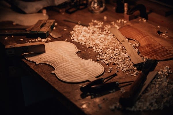 A desktop with wood and wood shavings as a violin is built