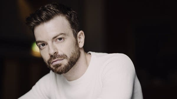 Poster A man in a white sweather leans on a dark surface
