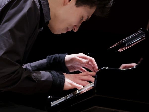 A man leans over a piano keyboard, playing with intensity.