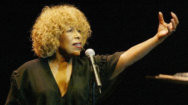 Poster A woman stands behind a microphone dressed in black